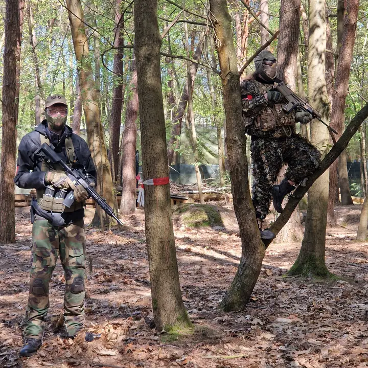 Twee spelers in camouflage tussen de bomen, een van hen klimt in een boom