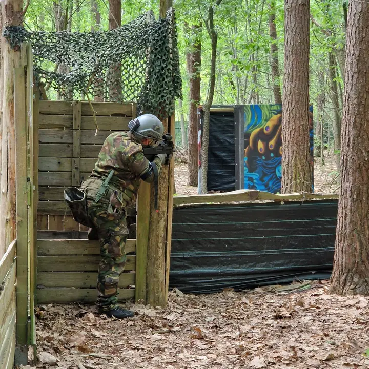 Speler kijkt over een houten schot met camouflagenet