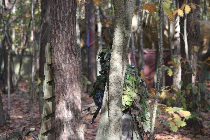 Speler in ghillie-pak verscholen tussen de bomen