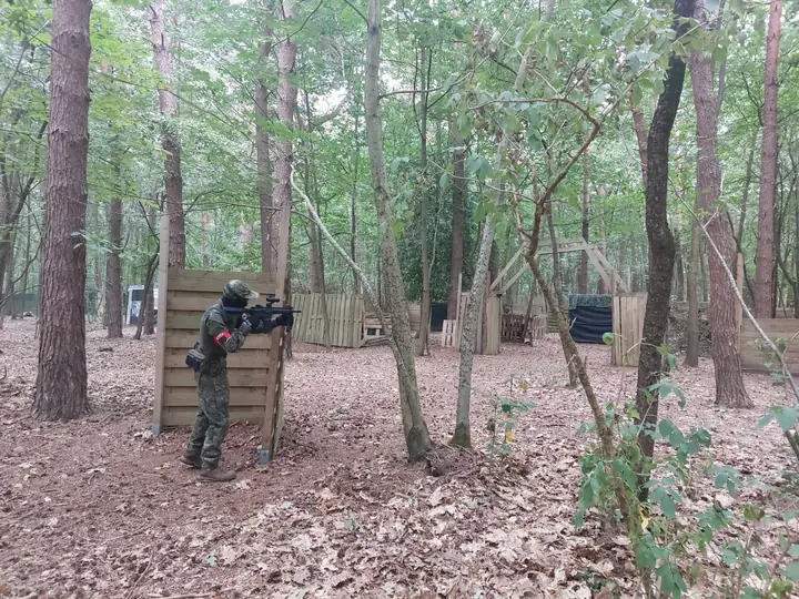 Speler in dekking bij een houten schot, met het terrein op de achtergrond
