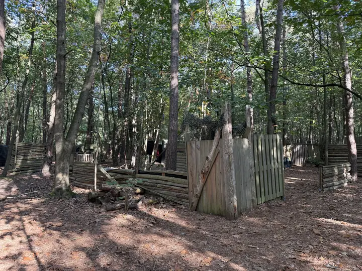 Houten fort van palen en planken met camouflagenet tussen de bomen